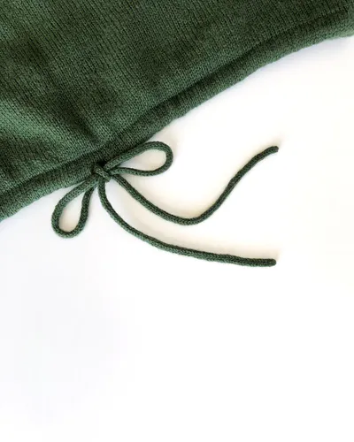 An icord hem of a green, hand knit sweater. The cord is tied in a cute bow.